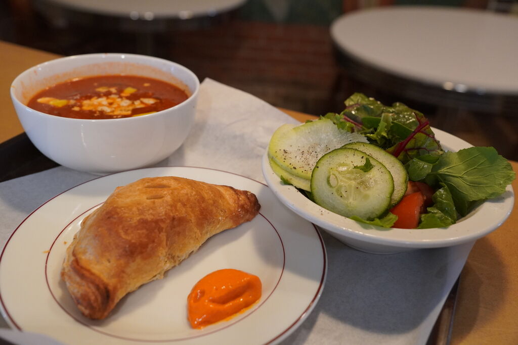Hand pie with chile sauce, a bowl of beef and vegetable soup, and a salad on a tray