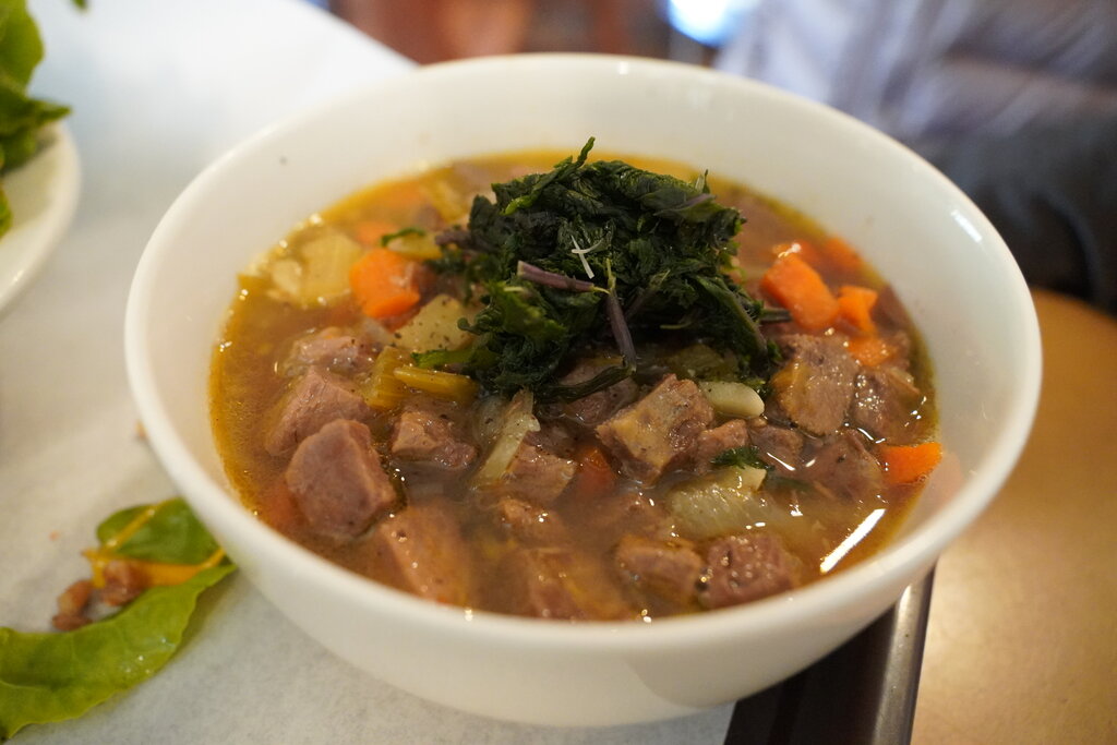 Bowl of beef and vegetable soup, topped with greens